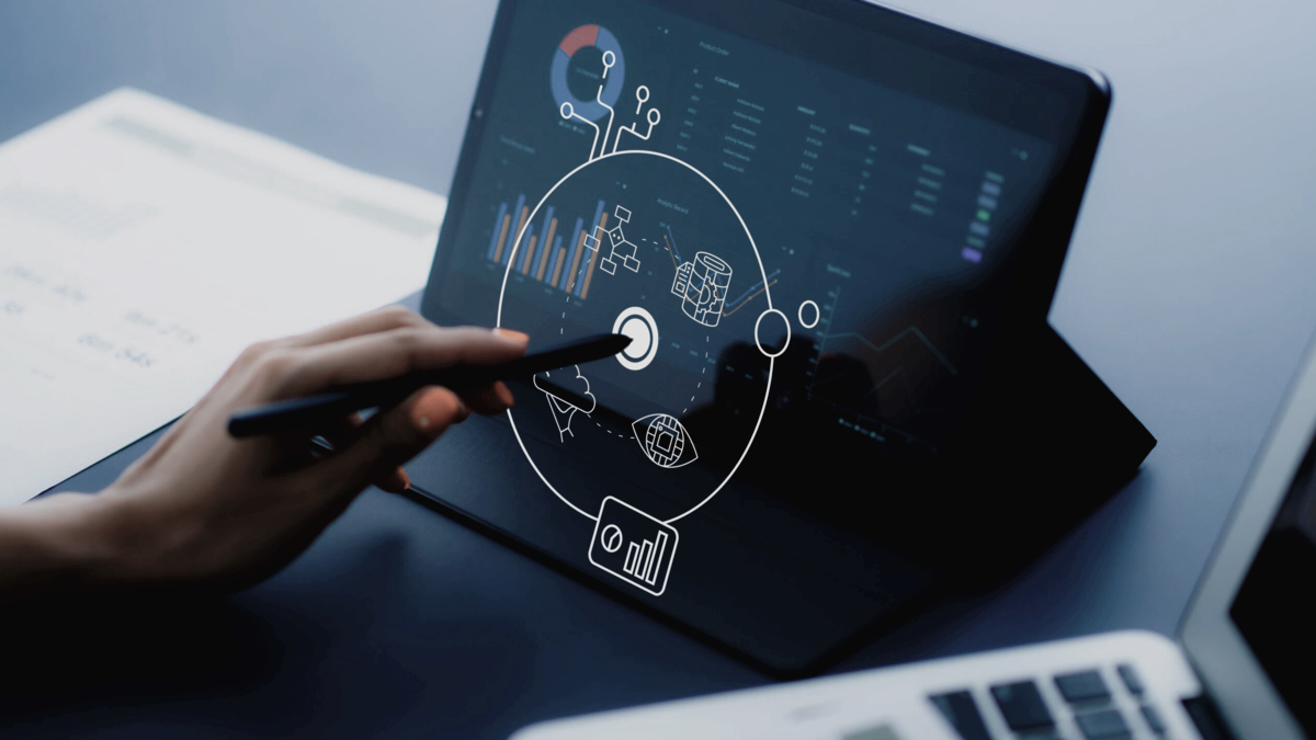 Hand holds touch pen and taps with it on graphic that floats in front of a tablet. Various graphs can be seen on the tablet.