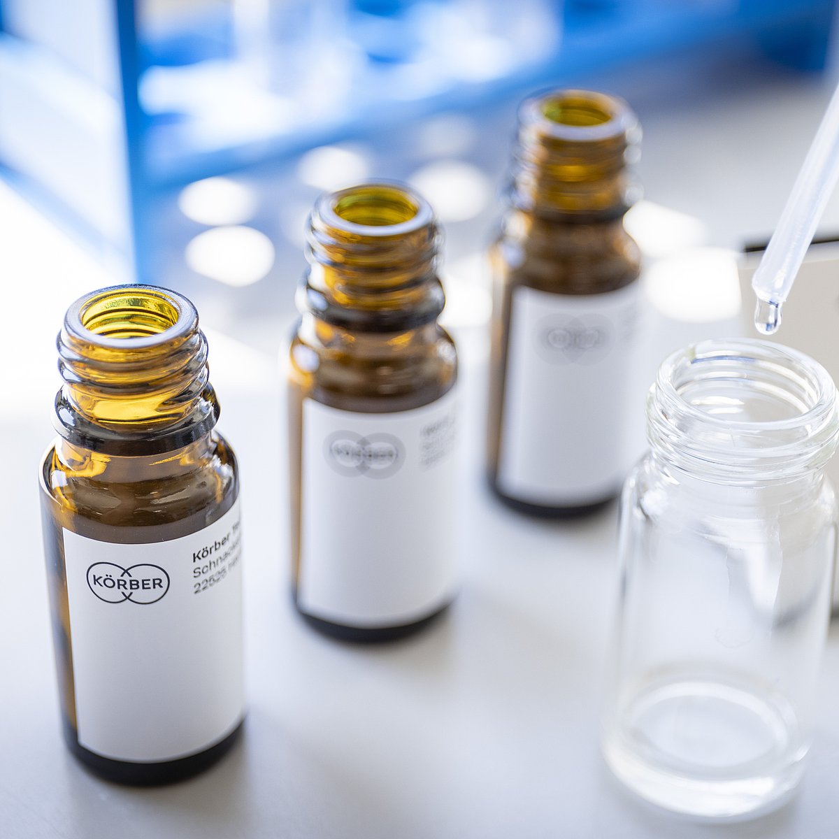 Small glass bottles of aroma with Körber's logo place behind a dropper with transparent liquid.