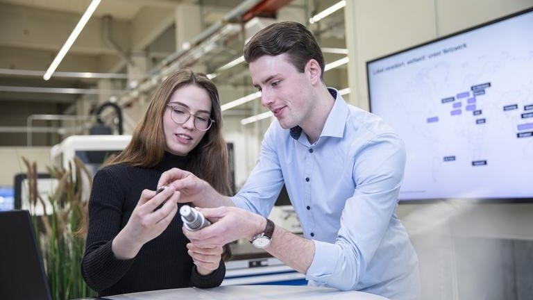 Zwei Wirtschaftsingenieurwesen Studenten von Körber Technologies betrachten gemeinsam ein Werkstück