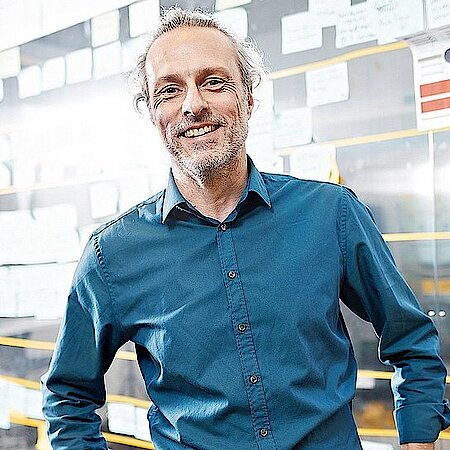 Man smiles at the camera and stands in front of a wall with sticky notes.