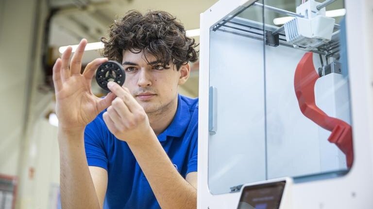 Ein Maschinenbaustudent von Körber Technologies betrachtet ein Werkstück aus dem 3D-Drucker