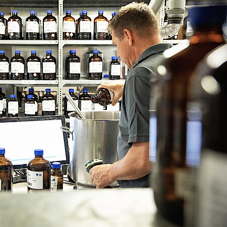 Man stands in front of shelf with aroma bottles and fills one of them into a pot.