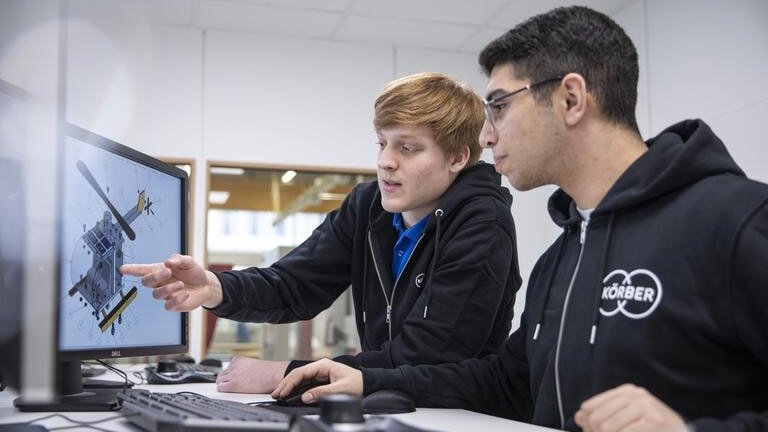 Zwei Auszubildende zum Technischen Produktdesigner betrachten eine technische Zeichnung auf dem Computerbildschirm