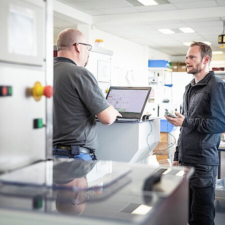 Two men are talking, one is holding a measuring instrument.