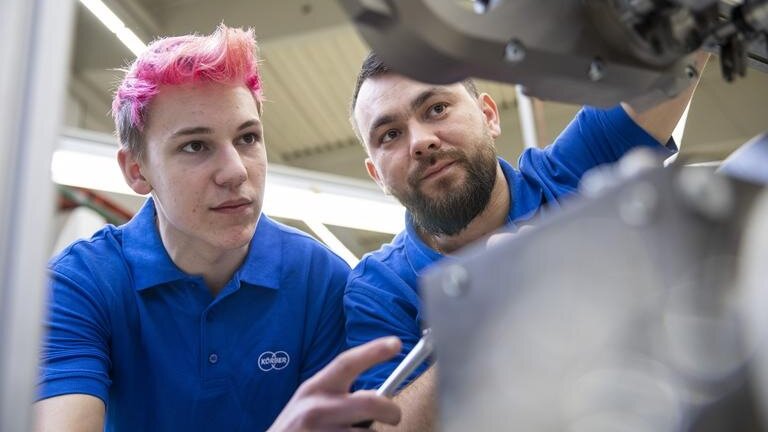 Ein Ausbilder zeigt einem Auszubildenden zum Industriemechaniker etwas an einer Maschine